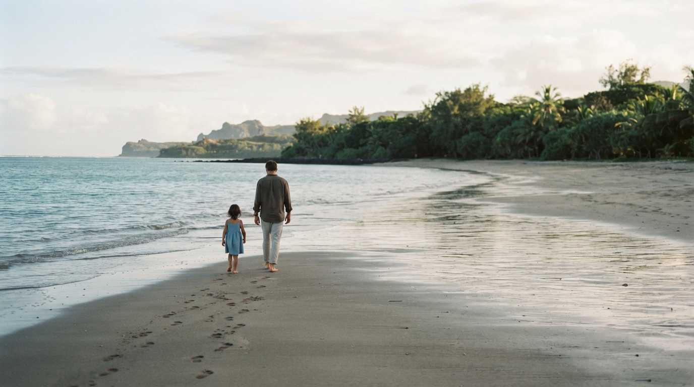 An adult and a child walking along a quiet beach, seen from behind.